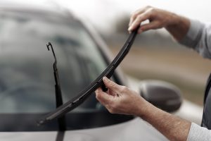 Close-up. Selective focus on the hands of a man driver, holding new brand windscreen wipers and replacing them, mounting on the windshield car on outdoors parking lot of a car station. Car maintenance